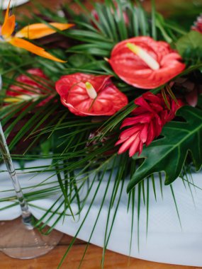 The decor of tropical flowers on the questionnaire table. Red anthurium, palm leaves, red ginger, strelitzia.