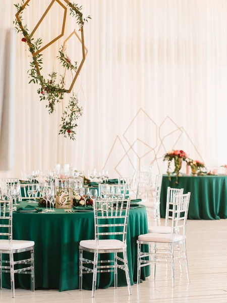 The decor of the wedding banquet hall with tables in emerald green, white drapery on the ceiling, and gold geometric decorative elements.