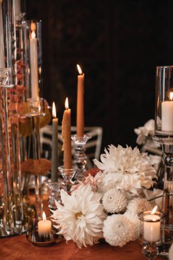 Floral decoration of the wedding table in white and orange colors. Orange tablecloth, burning candles in glass candlesticks, dahlias on a dark background.