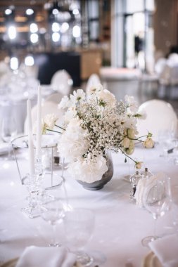 Wedding decor of a banquet table of snow-white color. White roses, peonies, gypsophila, white candles in glass candlesticks.