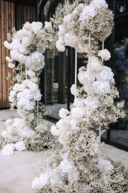 Wedding arch of white flowers against the background of a black panoramic window.