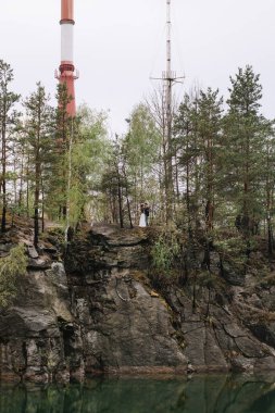 A clean mountain lake, on the other side of the cliff and a pine forest with a striped red and white radio came out. Forest and rocks are reflected in the water. Overcast weather.