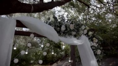 Ahşap düğün kemeri taze çiçekler ve beyaz bezle süslenmiş. Rüzgardan uzaklaşıyorlar. Yakın plan çekim. Yavaş çekim.