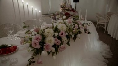 Düğün çiçeği aranjmanı masada pembe ve bej renklerde. Parti ziyafeti masasındaki güllerin çiçekli kompozisyonları. Yavaş çekim.