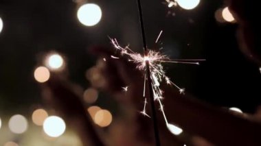Sparkler 'ı tutan eller. Havai fişek arka planda ışıklarla yanıyor.