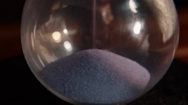 Hourglass. Close up. A pile of sand at the bottom of the hourglass, small grains of sand fall from above. Pass of time and waste time concept. 