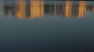 Su yüzeyindeki günbatımı renkleri göldeki gökdelenlerin yansıması. Balık oyunu.