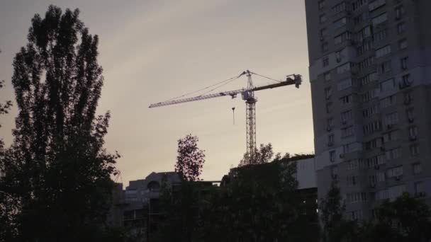 塔式起重机建造一座房子 建筑塔式起重机通过绿叶的低角度视图 住宅大楼正在建造中 — 图库视频影像