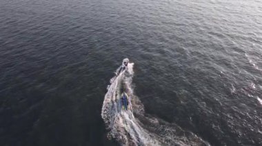 Bir sürat teknesinin şişme bir muz teknesini yüksek hızda çekerken görüntüsü. Video, tekneyi takip eden bir İHA tarafından çekildi. Deniz kenarında gezinti, deniz eğlencesi. 