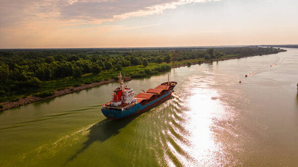 Aerial photography of a cargo transport ship seen on Danube at sunrise. Photo was taken from a drone at a higher altitude with camera lowered to keep the ship in focus.
