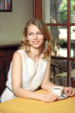Kafede bir fincan kahveyle oturan genç ve güzel bir kadın.