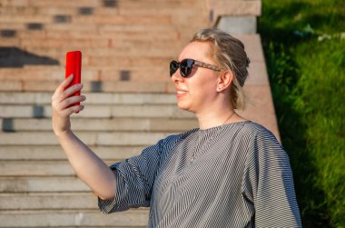 Sarışın, güneşli bir günde telefonda fotoğraf çeker, fotoğraf çeker ya da iletişim kurar.