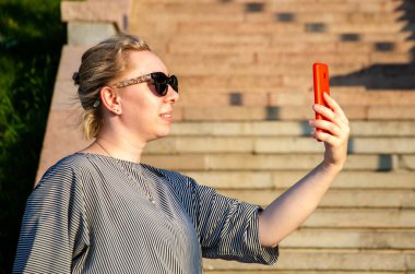 Sarışın, güneşli bir günde telefonda fotoğraf çeker, fotoğraf çeker ya da iletişim kurar.