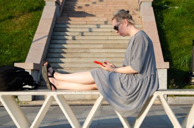 Bir kadın, bir yaz günü parkta otururken akıllı telefonundan internet alımları yapar ya da anında haberleşir.