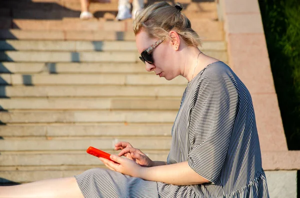 Bir kadın, bir yaz günü parkta otururken akıllı telefonundan internet alımları yapar ya da anında haberleşir.