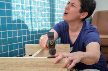 Koyu renk saçlı bir kadın acı içinde bağırıyor, çekiçle parmağına vuruyor, kendi evinde mobilyaları monte etmeye çalışıyor. Mobilya montajı, DIY