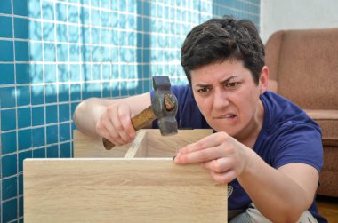 Koyu renk saçlı bir kadın elinde çekiçle çiviyi çok özenle çakıyor. Evde mobilyaları tek başına monte ediyor. Ev işi, DIY.