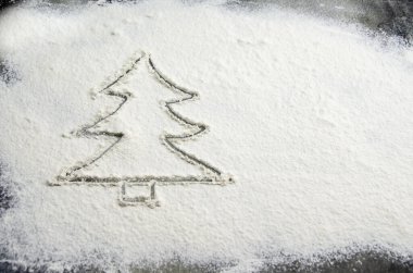 Masaya saçılmış un üzerine Noel ağacı çizilmiş. Mutfak masasının üzerindeki koyu beton zeminde undan yapılmış bir Noel ağacının silüeti. Tatil hazırlama konsepti, yeni yıl hediyeleri