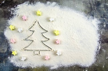 Masaya saçılmış un üzerine Noel ağacı çizilmiş. Mutfak masasının üzerindeki koyu beton zeminde undan yapılmış bir Noel ağacının silüeti. Tatil hazırlama konsepti, yeni yıl hediyeleri