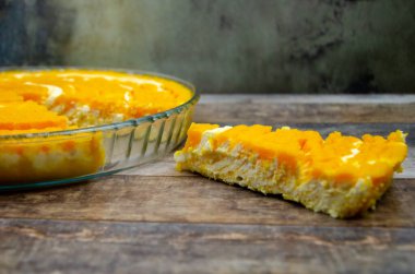 Balkabağı ve kremalı güveç. Bir dilim balkabaklı cheesecake, bir tepsi şekersiz turtanın yanında, ahşap masa arkaplanında portakal aromalı. Lezzetli beslenme tatlısı, üst görünüm, seçici odaklanma