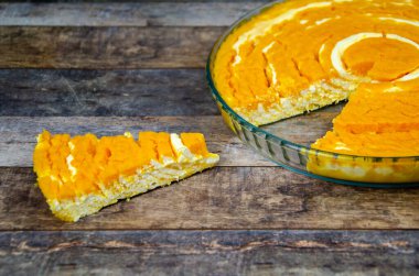 Balkabağı ve kremalı güveç. Bir dilim balkabaklı cheesecake, bir tepsi şekersiz turtanın yanında, ahşap masa arkaplanında portakal aromalı. Lezzetli beslenme tatlısı, üst görünüm, seçici odaklanma