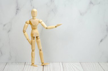wooden figurine of a man points with hand to empty space for text. Classic wooden mannequin in a demonstration pose, standing against a light background. Demonstration of a product or information