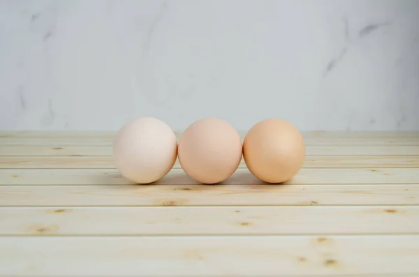 ベージュシェルの3つの鶏の卵は板の軽い木製の背景にあります テキスト用のスペース 農場有機製品 イースターの準備 ミニマルなコンセプト 木製の背景に連続した卵 — ストック写真