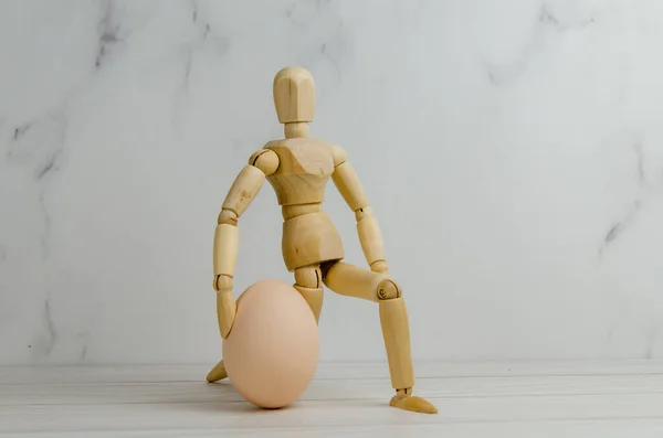 鶏の卵を持つ木製の男 マネキンが膝をついて卵を抱えた 創造的なイメージ アイデアのプレゼンテーション 創造的なプロセスの概念 テキストのスペース — ストック写真