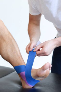 Yaralı erkek hasta ayağında mavi bant ile Kineziyoloji bandı tedavisi. Spor yaralanması kinesio tedavisi.
