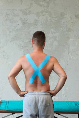 Sırtında ve omuzlarında kas bandı olan kaslı bir adam. Kinesioting, kinesiyoloji bandı - sırt ağrısı için başvuru.
