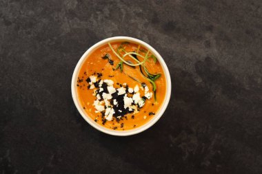 Beyaz peynirli havuç çorbası ve koyu arkaplanda siyah bir konteynır içinde mikro yeşillikler. Sağlıklı yemek teslimatı kavramı.