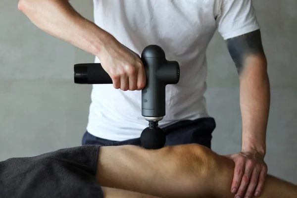 マッサージ パーカッション デバイスを搭載したマッサージ レッグ マッサージテーブルの上に横たわるスパ治療に筋肉運動選手のマッサージ銃の打楽器 — ストック写真