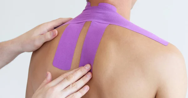 Kineziyoloji bandı. Hastanın boynundaki kineziyoloji bandı. Beyaz arka planda genç bir erkek atlet. Travma sonrası rehabilitasyon, spor fizyoterapisi, iyileşme konsepti, alternatif tıp.