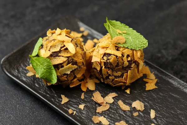 Vegan raw sweet balls on a black plate. Natural sweets from nuts and dried fruits in flakes, cocoa and sesame seeds, close-up. Healthy chocolate truffles. Sugar-free and gluten-free sweets, raw food.