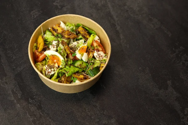Healthy bowl with fried squid, egg, tomatoes, cucumbers, lettuce, cream cheese and flax seeds salad isolated on dark background. Food delivery service and daily ration concept.