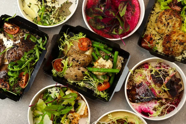 Günlük beslenme için paket restoranlarda sağlıklı yiyecek teslimatı. Günlük yemeklerle dolu konteynırlar - et, balık, sebze ve kanun yağlı atıştırmalıklar gri arka planda.