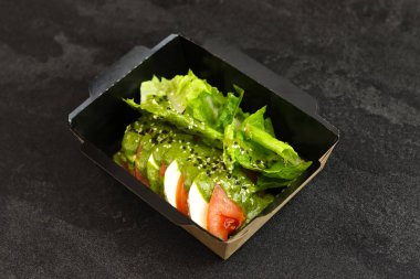 Mozarella soslu taze İtalyan caprese salatası ve koyu arka planda siyah paket servis kutusunda domates. Sağlıklı yemek teslimatı kavramı.