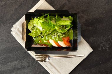 Mozarella soslu taze İtalyan caprese salatası ve koyu arka planda siyah paket servis kutusunda domatesler. Sağlıklı yemek teslimatı kavramı.