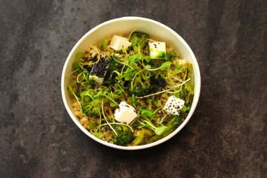 Bulgur, brokoli, yeşillik ve koyu arka planda izole edilmiş feta peynirli vejetaryen sağlıklı kase. Sağlıklı gıda dağıtım hizmeti ve günlük istihkak kavramı.