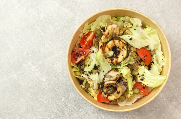 Fish salad. Fresh vegetable salad with baked fish fillet. Fish salad with fried fillet and fresh vegetables in eco paper bowl on gray background. Food delivery service and daily ration concept.