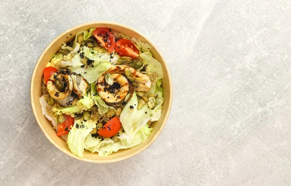 Fish salad. Fresh vegetable salad with baked fish fillet. Fish salad with fried fillet and fresh vegetables in eco paper bowl on gray background. Food delivery service and daily ration concept.