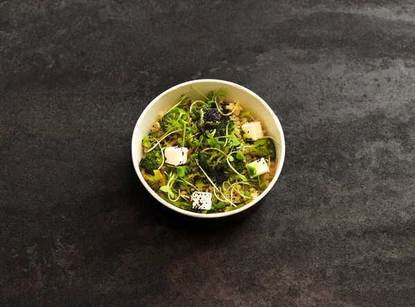 Vegetarian healthy bowl with bulgur, broccoli, greens and feta cheese isolated on dark background. Healthy food delivery service and daily ration concept.
