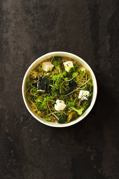 Vegetarian healthy bowl with bulgur, broccoli, greens and feta cheese isolated on dark background. Healthy food delivery service and daily ration concept.