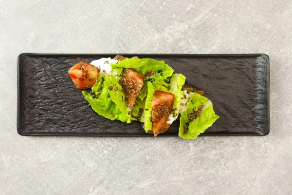 Gri arka planda siyah tabakta domates, tavuk ve krem peynirli taze marul salatası yaprakları. Sağlıklı restoran yemekleri konsepti. Metin için boş alan.