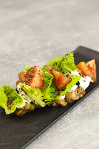 Gri arka planda siyah tabakta domates, tavuk ve krem peynirli taze marul salatası yaprakları. Sağlıklı restoran yemekleri konsepti. Metin için boş alan.