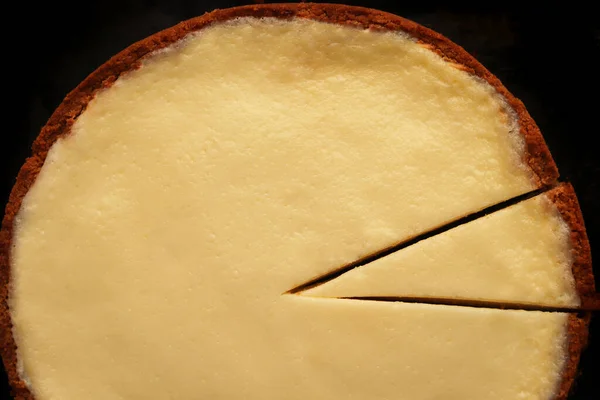 Creamy plain cheesecake texture with crust on a black background.