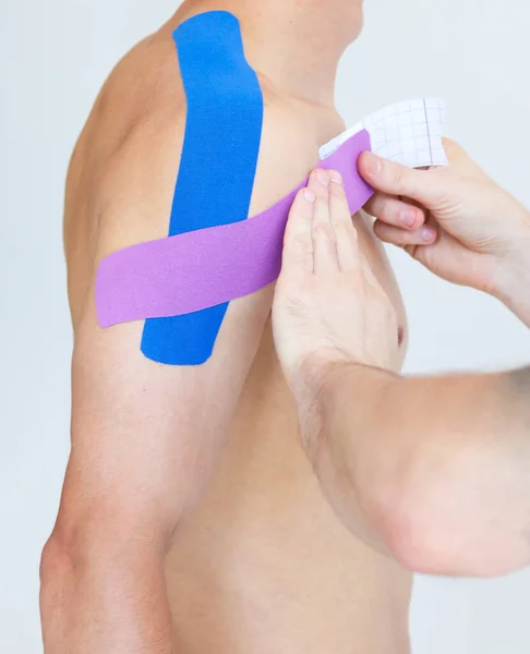 Kinesiology taping. Physical therapist applying kinesiology tape to patient shoulder. Male therapist treating injured shoulder of male athlete. Post traumatic rehabilitation, sport physical therapy.