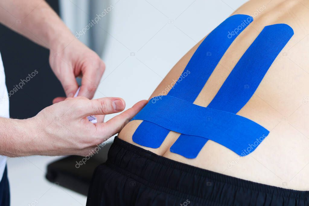 Physical therapist applying kinesio tape on male patient's lower back. Kinesiology, physical therapy, rehabilitation concept.