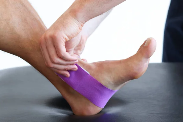 Kinesiology taping treatment with purple tape on male patient injured foot. Sports injury kinesio treatment.