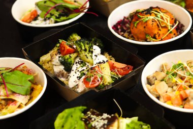 Günlük beslenme için paket restoranlarda sağlıklı yiyecek teslimatı. Günlük yemeklerle dolu konteynırlar. Siyah arka planda et, balık, sebze ve kanun yağı atıştırmalıkları..